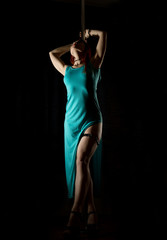 sexy woman pole dancer in a long turquoise dress with a slit on a dark background