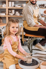 kid making ceramic pot on pottery wheel with teacher in workshop