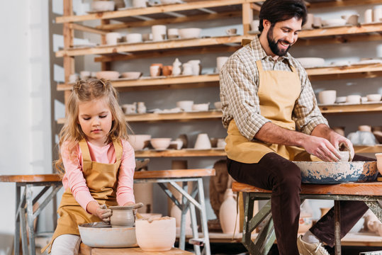 kid making ceramic pot on pottery wheel with teacher near in workshop