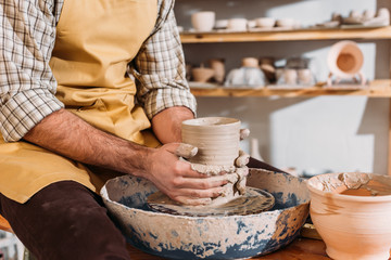 partial view of male hands with ceramic pot on pottery wheel