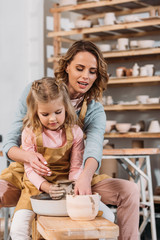 mother and daughter making ceramic pot on pottery wheel together