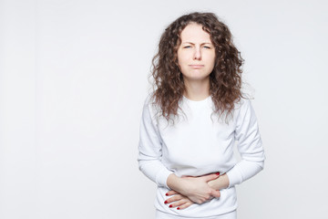 Bad experience at new restaurant. Studio shot of young Caucasian woman having painful expression holding hands on stomach, feeling sick because of diarrhea, going to throw up. Human health concept.