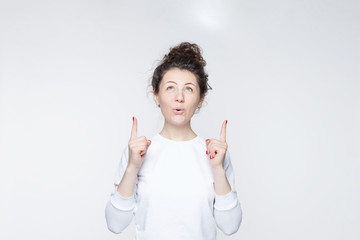Portrait of happy smiling woman points with both hands up, advertises something as stands against...