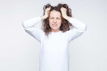 Headshot of young Caucasian female with annoyed expression, scratches head and screams loudly,...