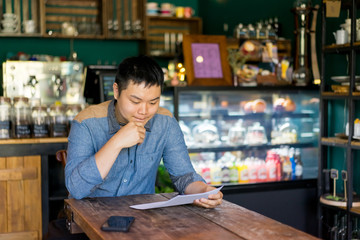 Pensive Asian male customer reading menu while choosing dish for business lunch. Or young...