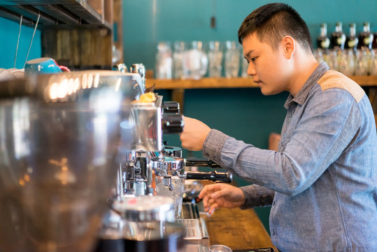 Serious Young Asian Barista Working In Coffee House. Busy Guy Concentrated On Coffee Making. Service Occupation Concept