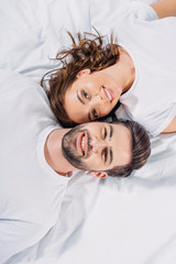 Obraz na płótnie Canvas overhead view of young smiling couple in love looking at camera while lying on bed together