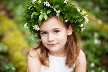 Beautiful  little girl in a white dress  in the spring wood. Portrait of the pretty little girl with a wreath from spring flowers on the head.