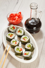 Sushi rolls with rice on ceramic plate, chopsticks, glass bottle with soy sauce and pickled ginger in a bowl
