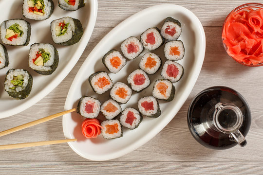 Different  sushi rolls on ceramic plate, chopsticks, glass bottle with soy sauce and pickled ginger in a bowl