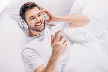 Obraz premium overhead view of smiling man in headphones using smartphone in bed