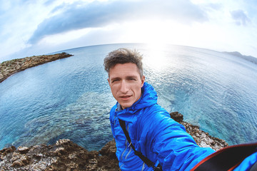 young man in blue jacket make selfie photo on the beach at sunset