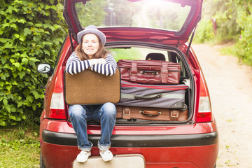 happy girl with old suitcases sits on the trunk of the car and waits for departure