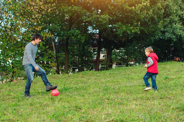 Young father with his little son playing football on green grassy lawn.