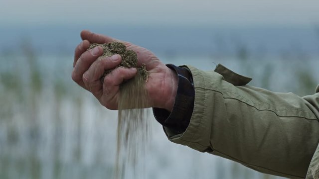 A man holding some dirt in his hand in front of a lake.