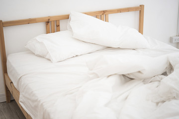 Fototapeta na wymiar white bedding sheets and pillow in white bedroom. Messy and crumpled bed concept.