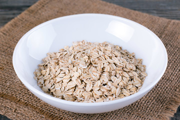 A white bowl of raw oat-flakes