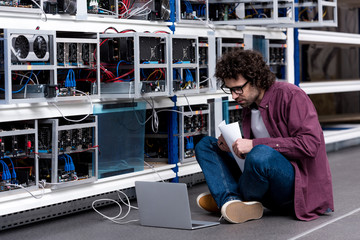 young computer engineer working while sitting on floor at cryptocurrency mining farm