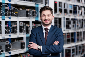 smiling young businessman with crossed arms at cryptocurrency mining farm