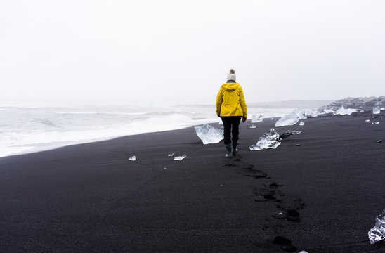 Woman walking away on the black sand beach with ice - Powered by Adobe