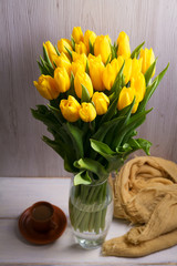 Bouquet of spring tulips flowers in vase on white wooden background. Yellow tulips