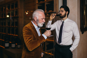 Winemakers in wine cellar holding glass of red wine and checking it. Sommeliers testing wines in winery. 