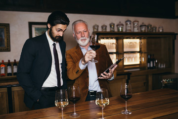 Winemakers in wine cellar holding glass of red wine and checking it. Sommeliers testing wines in winery. 