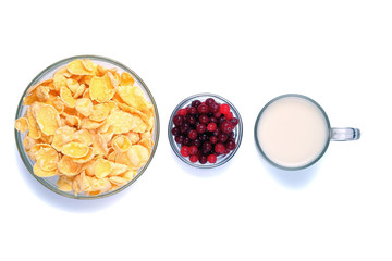 Bowls with cornflakes and cranberrries and cup with milk isolated on white. Healthy food.