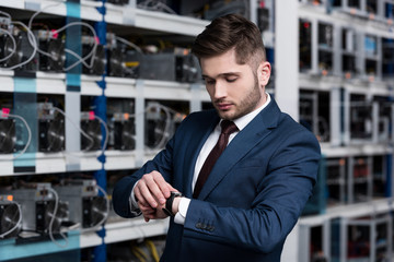 handsome young businessman looking at wristwatch at ethereum mining farm