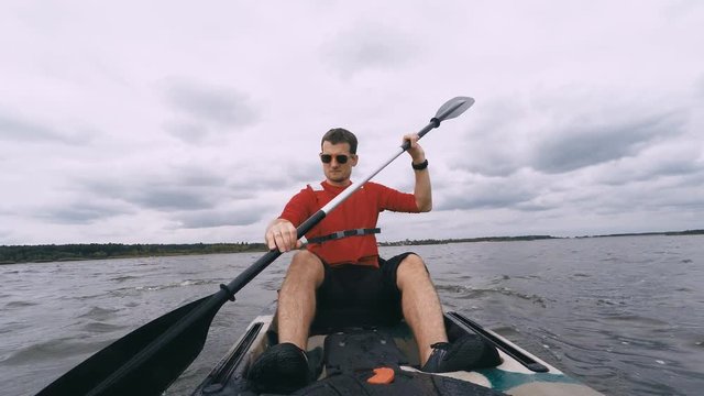 Man kayaking on open water. Young guy swims in kayak or canoe on a lake looking at camera. View from front of kayak. Inspiring water sport in beautiful landscape. Shot with GOPRO HERO4 4K UHD video.