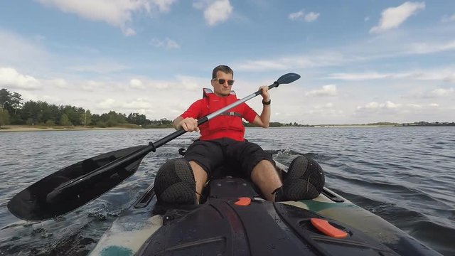 Man kayaking on open water. Young guy swims in kayak or canoe on a lake looking at camera. View from front of the kayak. Inspiring water sport in beautiful landscape. Shot with GOPRO HERO4 HD video.