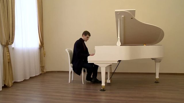 young pianist with glasses playing on a white grand piano