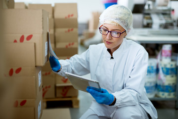 Young beautiful focused female worker in sterile cloths using a tablet to check correction of...
