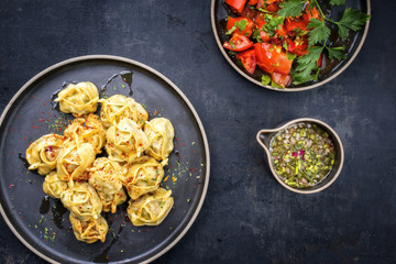 Traditional Kazakh manti steamed with mincemeat and tomato salad as top view on a modern style plate