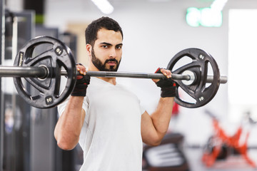 Fototapeta na wymiar Bearded muscular man wears white t-shirt have workout with barbell in the gym