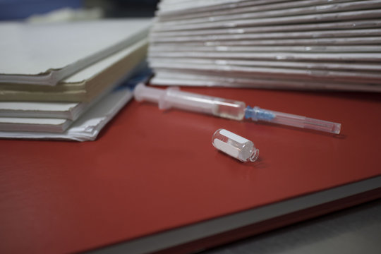 syringe with an open ampoule on a red notebook on a metal medical table