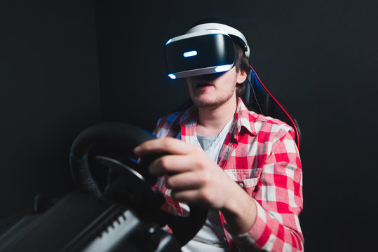Portrait of a young man who plays a race in virtual reality. Gamer with VR eyeglasses plays racing on the car simulator. Isolated on black background
