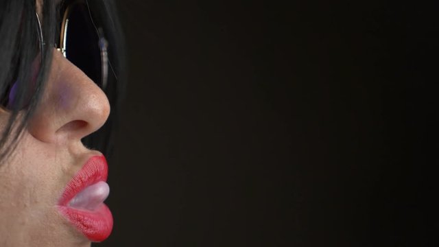Hot brunette in round sunglasses, chewing gum and blowing a bubble. 4k, slow motion.