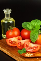 Tomatoes and herbs on a kitchen board. Preparation of healthy food. Raw vegetables. On a black background.