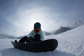 snowboarder buckle up the binding on winter ski resort slope