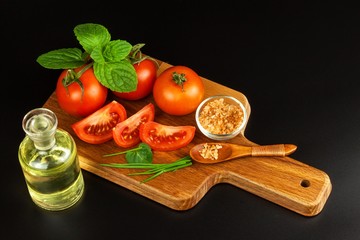 Tomatoes and herbs on a kitchen board. Preparation of healthy food. Raw vegetables. On a black background.