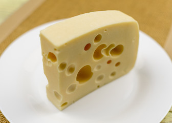 A piece of cheese with holes  on a white plate.