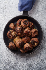 Traditional swedish beef meatballs served in one portion black cast iron pan, handle wrapped in blue towel. Textured background.