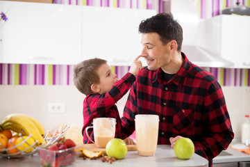 Cute little boy is bopping his fathers nose in the bright kitchen.