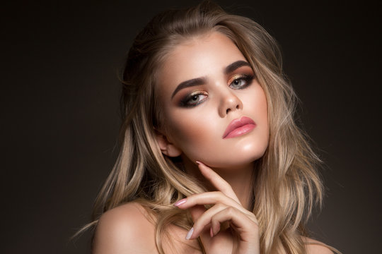 Glamour portrait of beautiful girl model with makeup and romantic wavy hairstyle. Fashion shiny highlighter on skin, sexy gloss lips make-up and dark eyebrows.