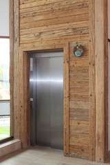 Metal elevator door in modern building with wooden walls. Hall with wooden wall around of lift closed door. vertical image. 