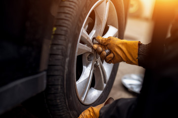 Auto mechanic man with electric screwdriver changing tire outside. Car service. Hands replace tires on wheels. Tire installation concept.