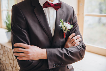 guy in a suit and a bow tie is standing near the window, hands clasped