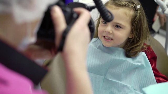 Child girl in dental clinic in dentist chair with doctor taking photos of teeth