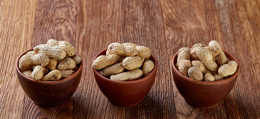 Three wooden bowls of unpeeled peanuts over rustic wooden background closeup, selective focus